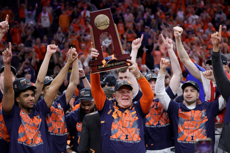 The University of Illinois basketball team flank their coach as he holds a trophy above his head.