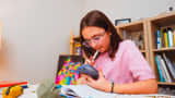 Preteen girl at desk solving homework with AI chatbot. 