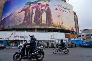 Motorbikes drive past a billboard depicting Iran’s late Supreme Leader Ayatollah Ali Khamenei, center, handing the country’s flag to his son and successor Ayatollah Mojtaba Khamenei